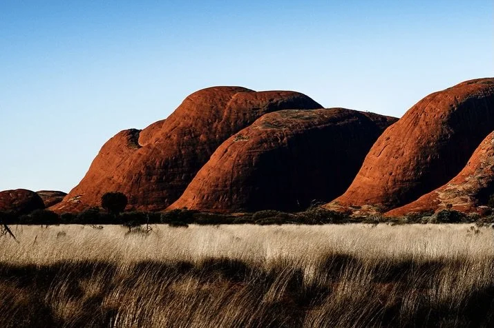 Kata Tjuta, Central Australia, afternoon light.
These monoliths roll across the ochre and rust-coloured landscape as if scattered from the heavens. As the sun sets, deep shadows creep along their curves, while the silence hums with ancient energy.

T