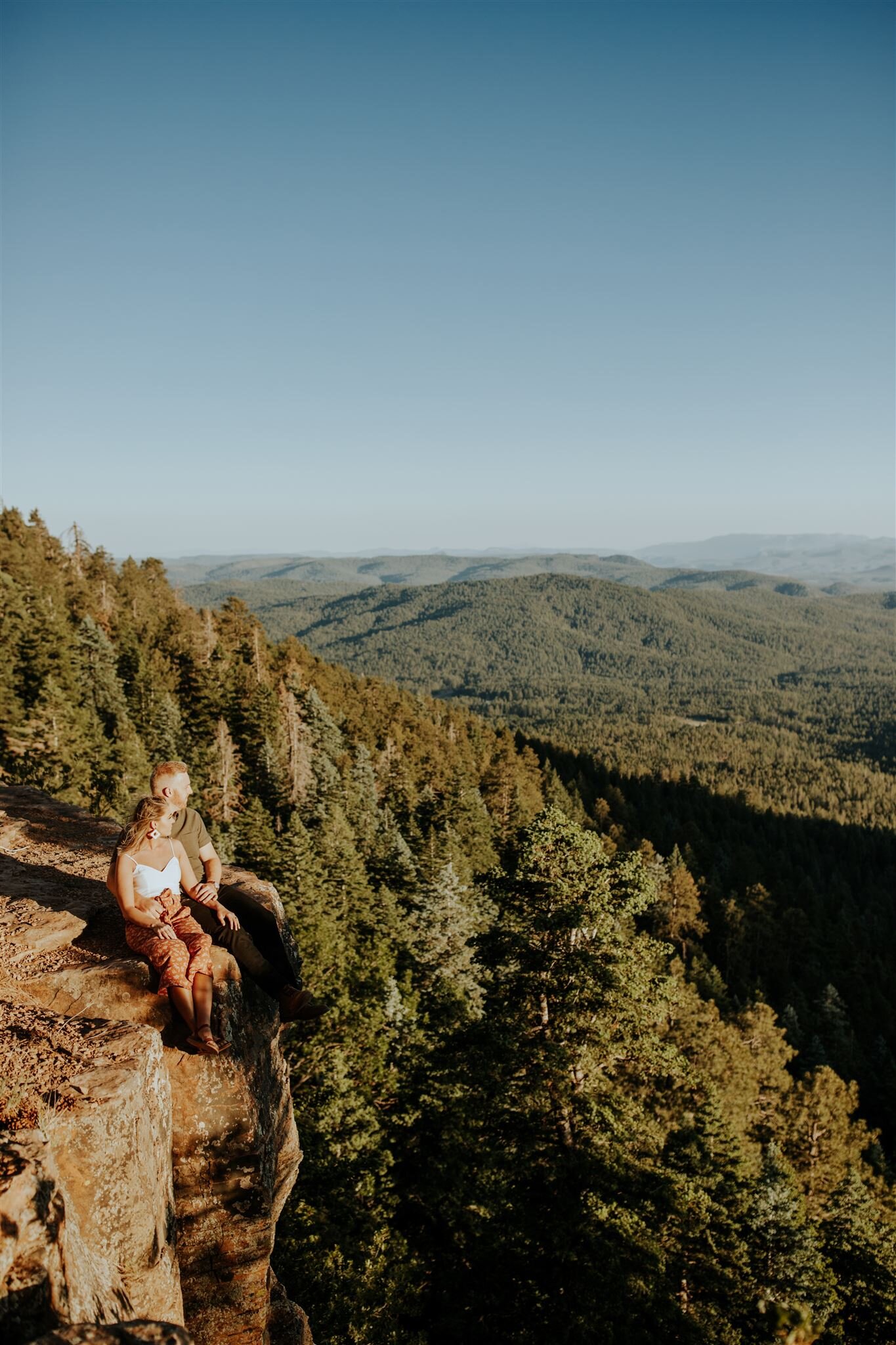  couple overlooking the dense forest on a cliff with sun in their eyes 