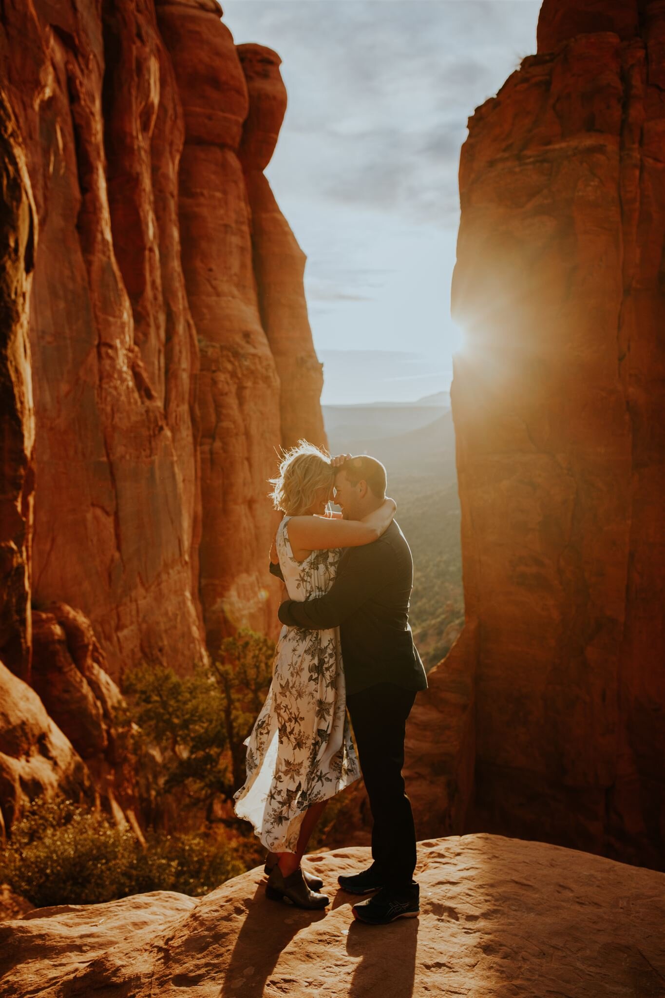  adventurous couple at end of hike in fancy outfits with sun flare behind them 