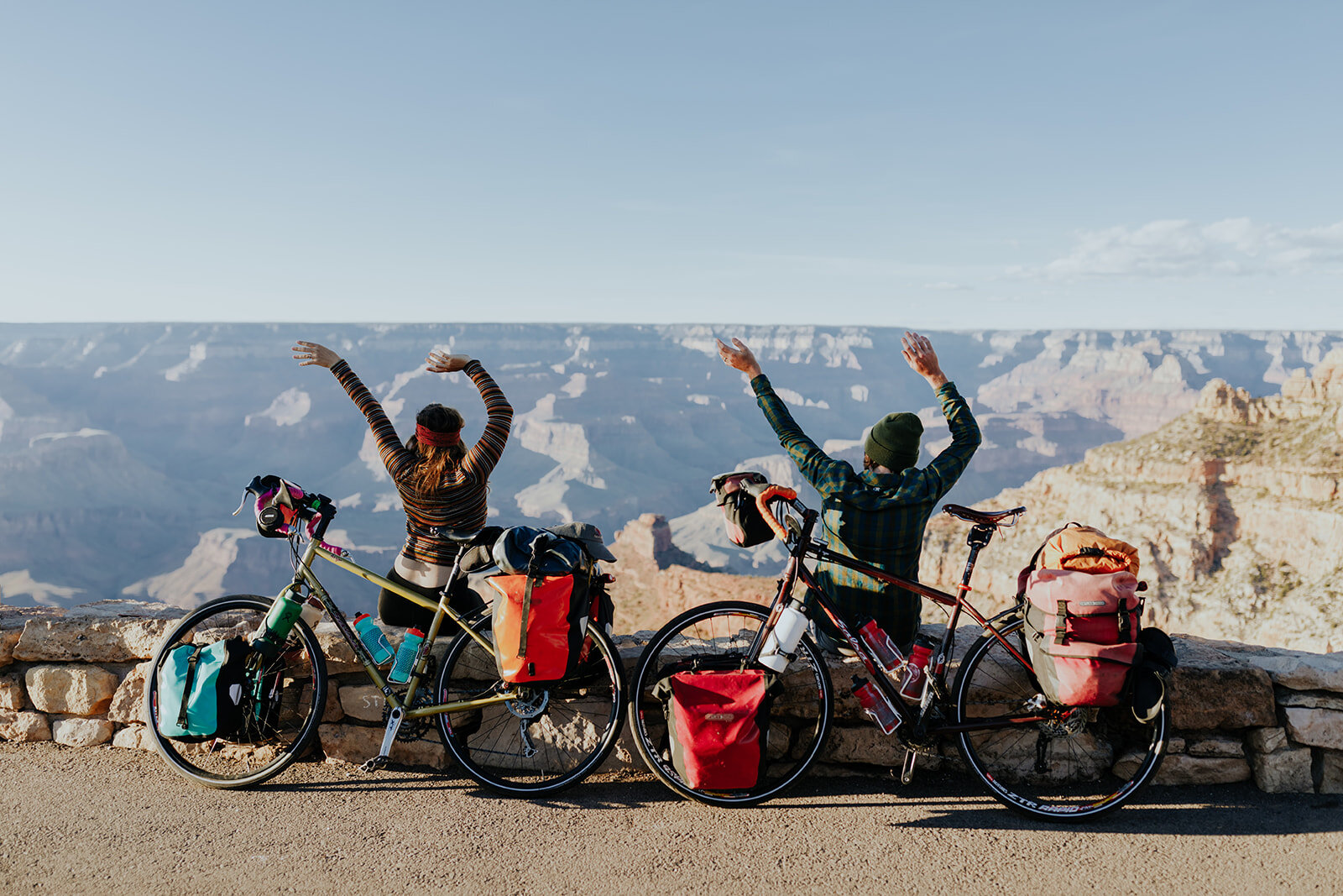  a couple with their bikes overlooking the grand canyon with their hands in the air after completing their exploring for the day and ending their adventure with pictures 