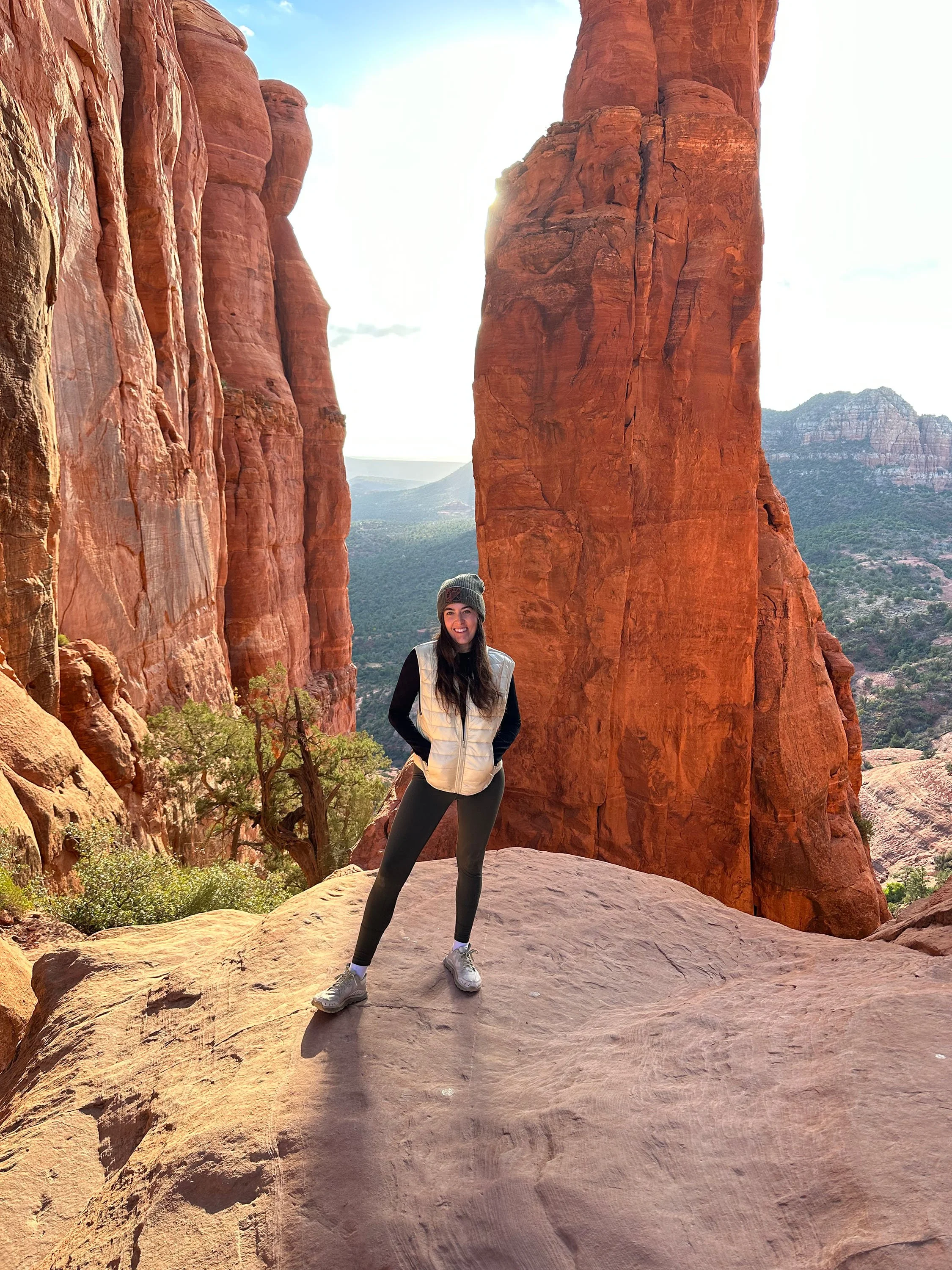 Person posing between red rock formations in a desert landscape with distant mountains.