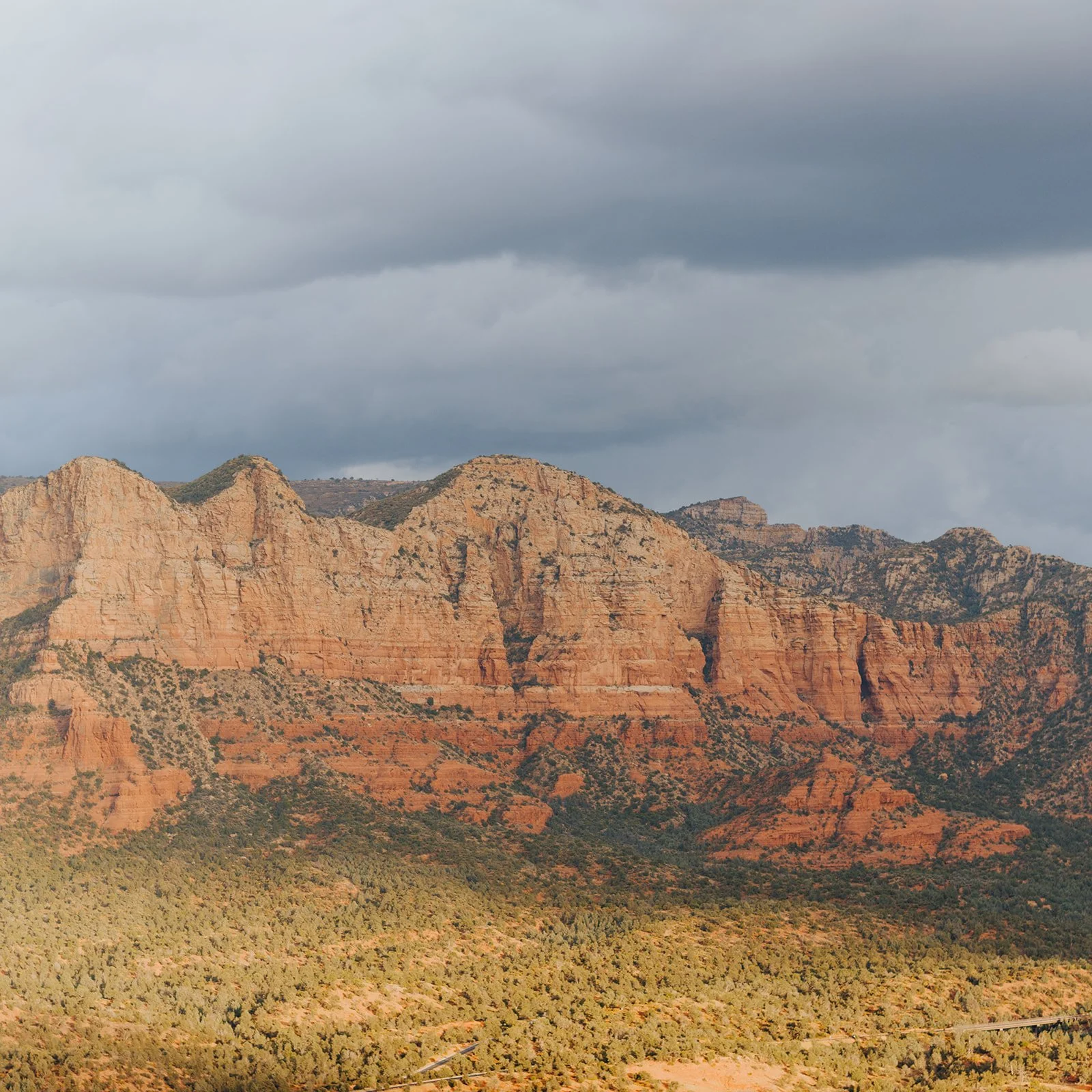 Landscape of red rock formations and forest under a cloudy sky.