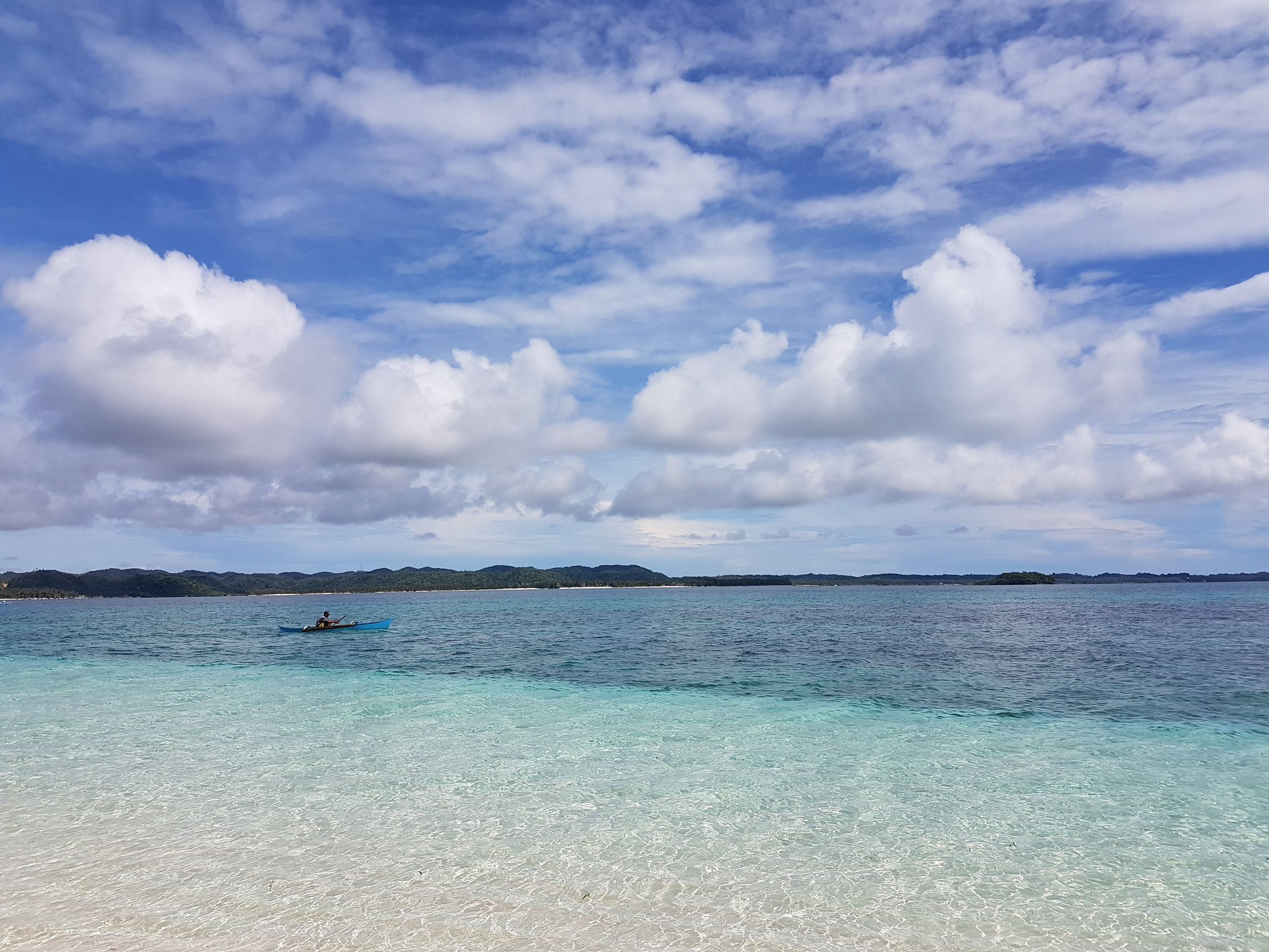 A fisherman on a small blue boat blends in with the equally blue green waters surrounding Naked Island in Siargao, Surigao del Norte.