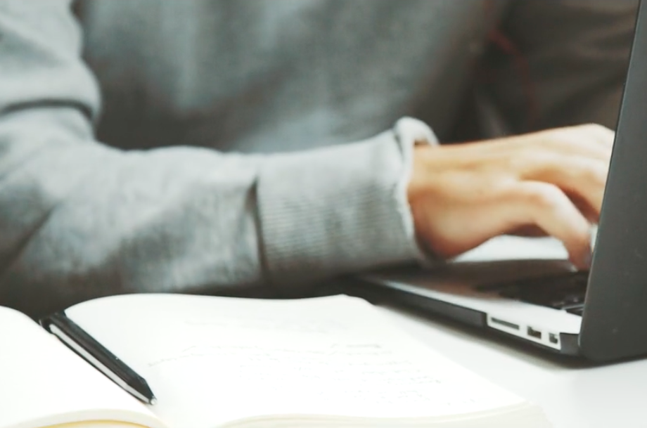 Person working at laptop with pen and blank sheet of paper.