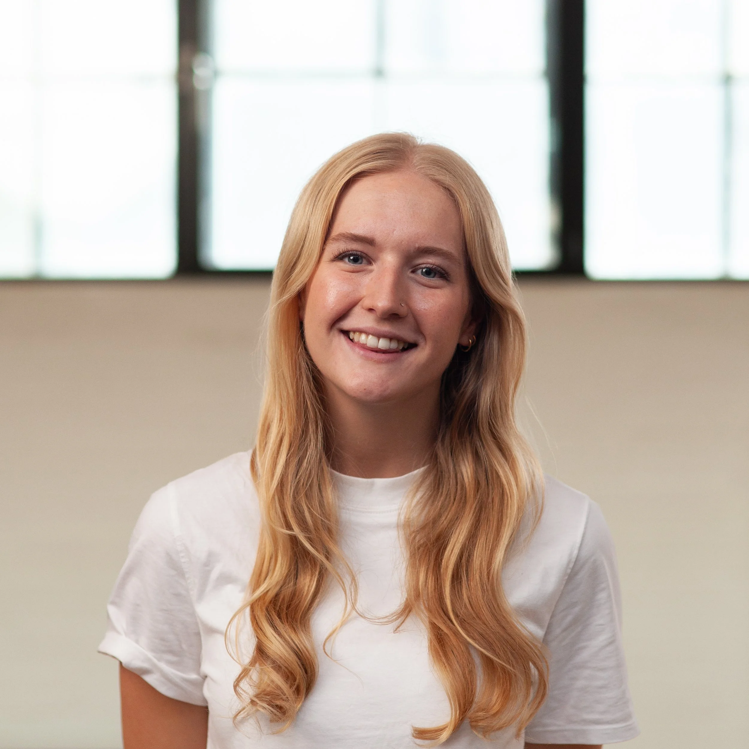 A smiling Naomi Kempson standing in front of a wall.