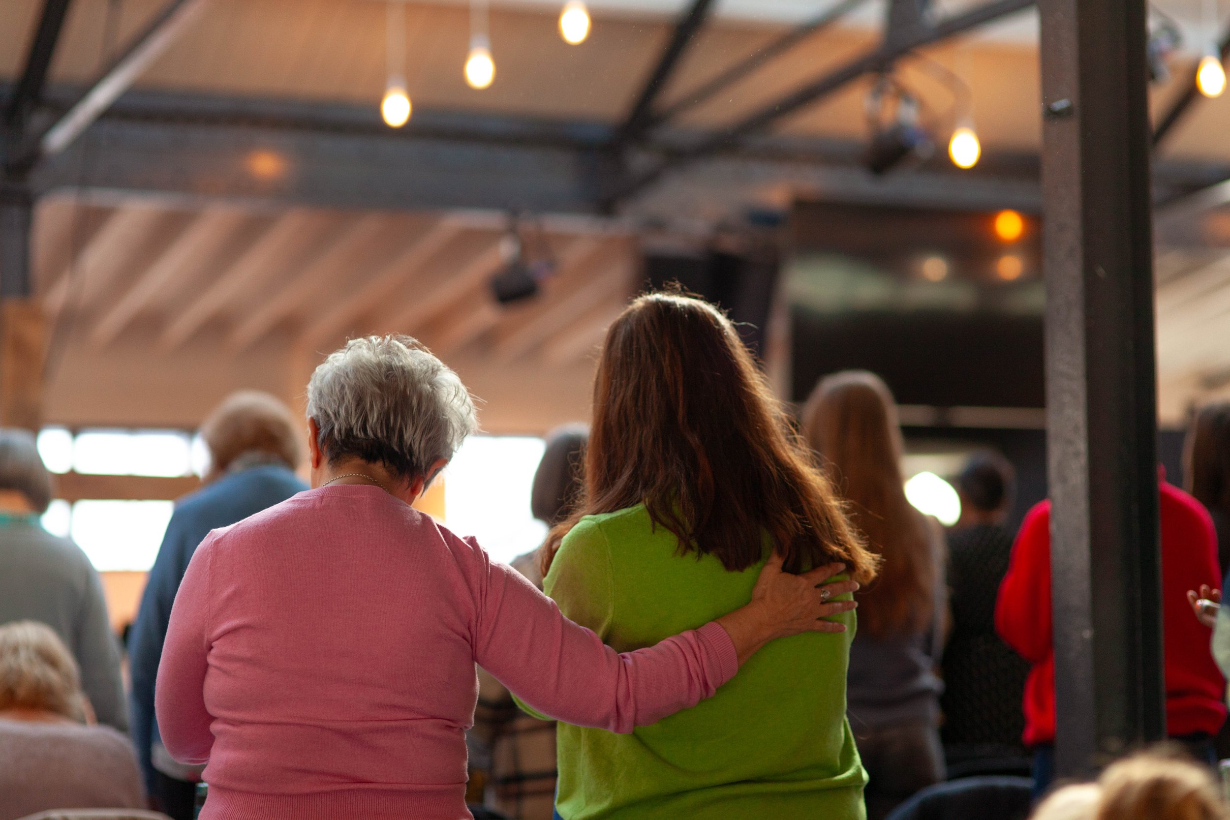 An older lady putting her hand on another lady in the act of prayer and pastoral care.