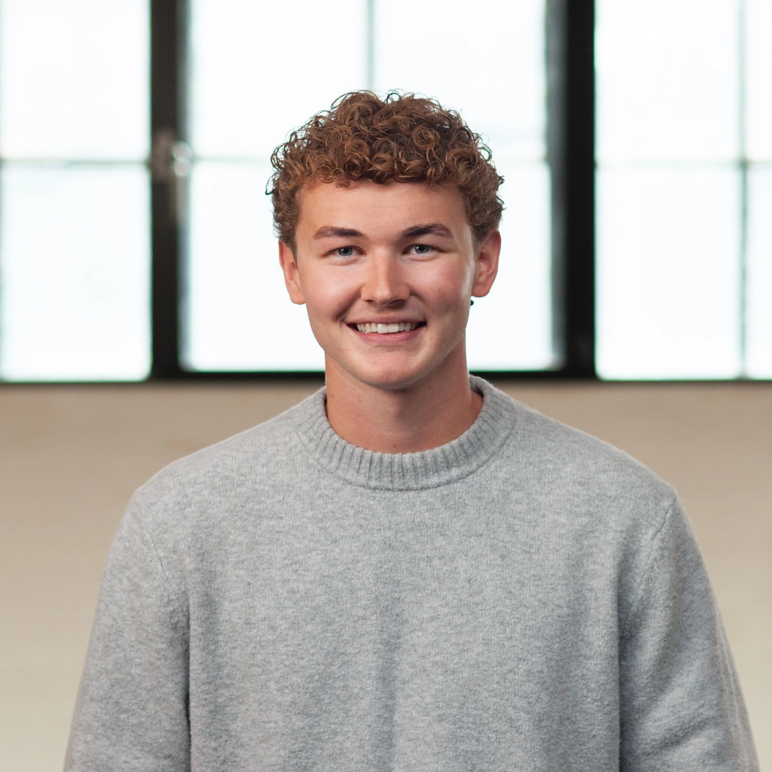 A smiling Sam Gowen standing in front of a wall.