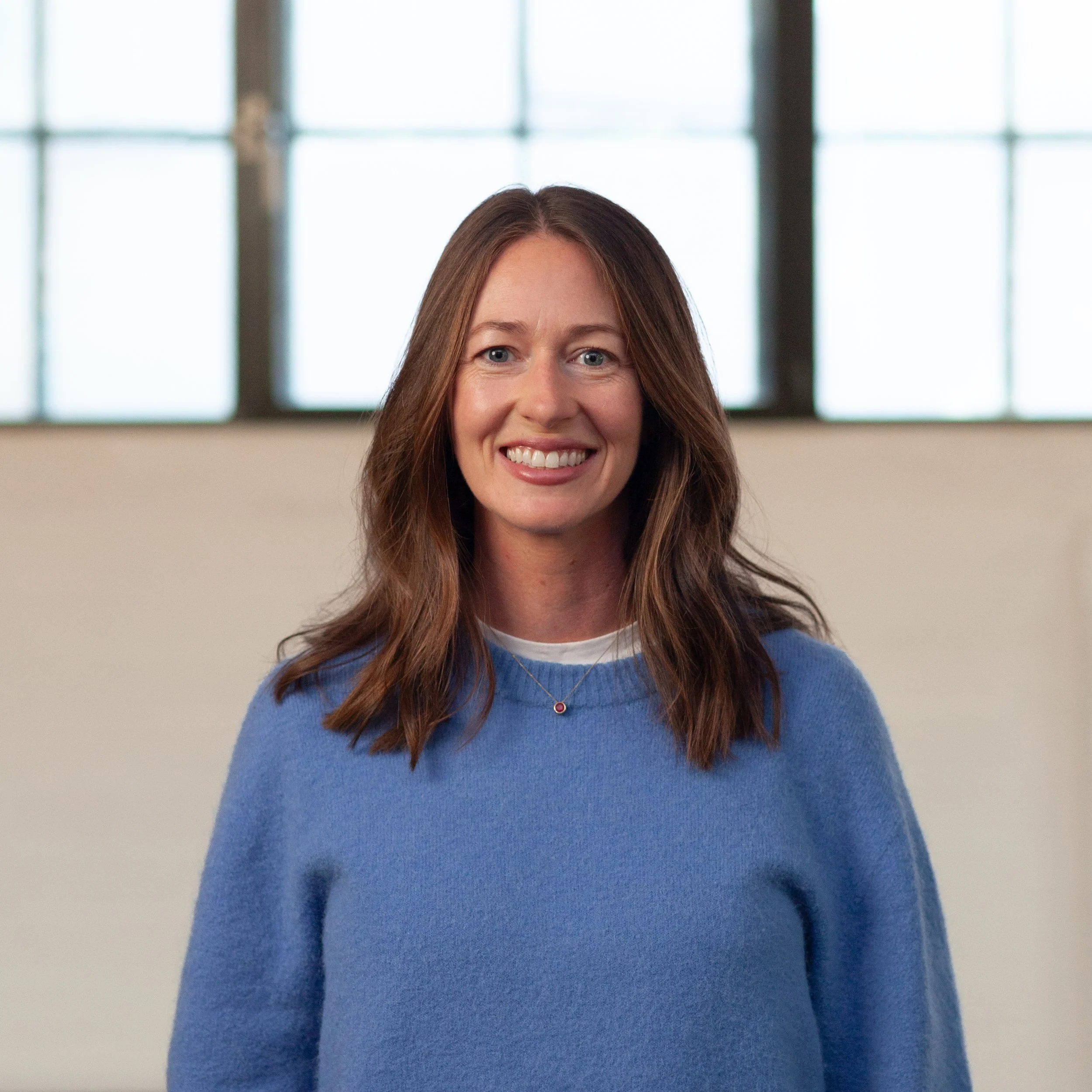 A smiling Christine Proctor standing in front of a wall.