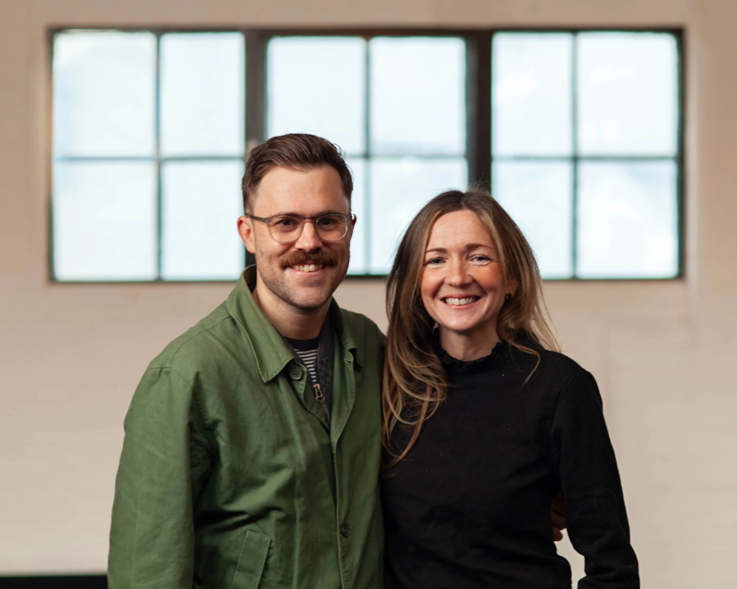 Jonny and Amy Hughes standing in front of a wall.