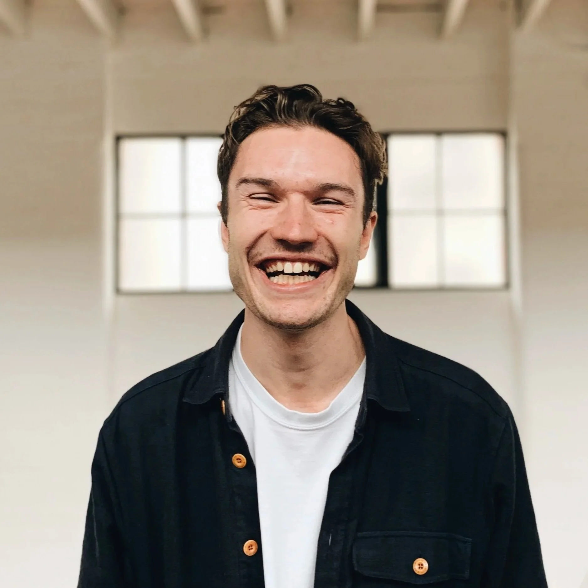 A smiling Sam Watkins-Smith standing in front of a wall.