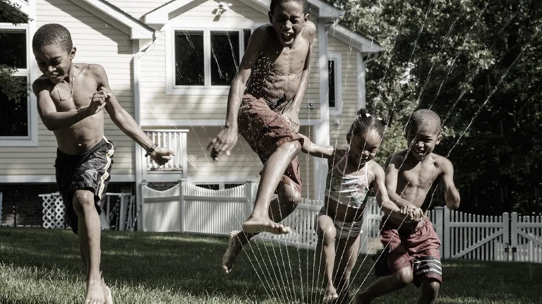 Three children playing in sprinkler