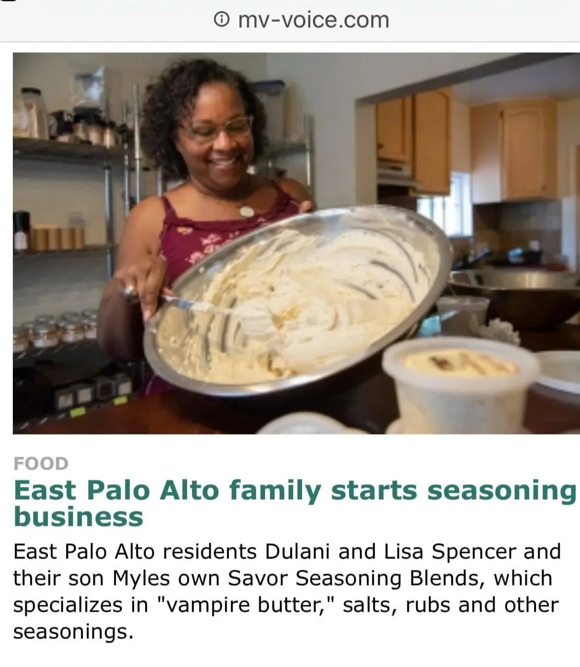 A woman with glasses and curly hair smiling while holding a bowl of seasoning or batter in a kitchen setting.