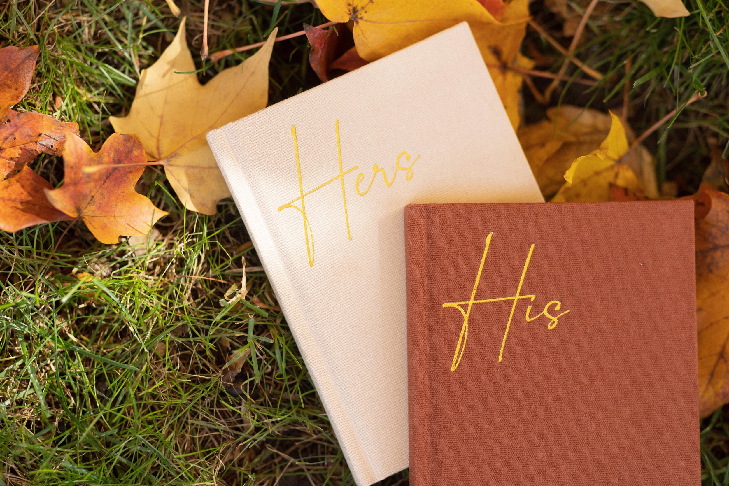 His and hers vow books set against Fall leaves.