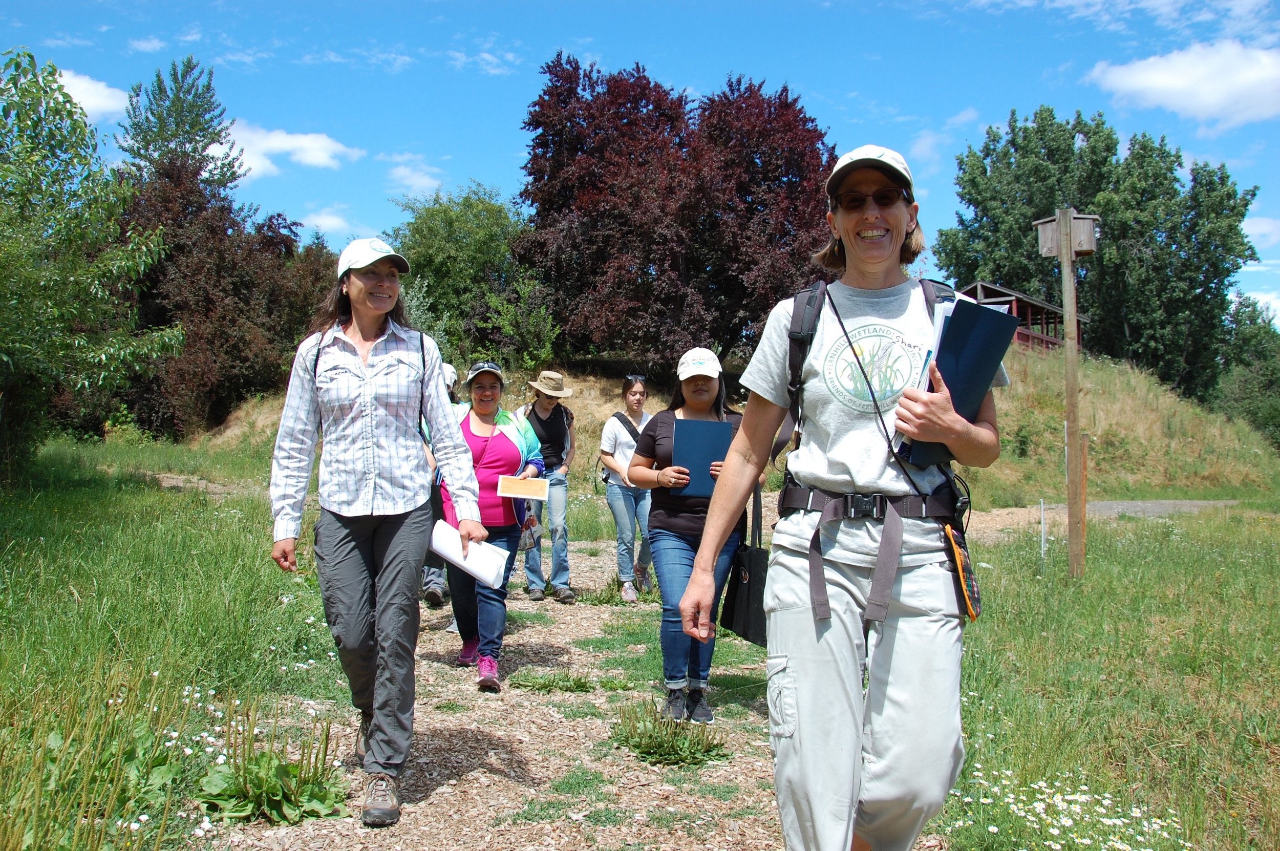  Local ecologists, Lorena (left), and Shari (right), lead members of the group through Jackson Bottom Wetlands. The blue folders contain facts and information that Naturalists will share with their walking groups, both in English and Spanish, as they
