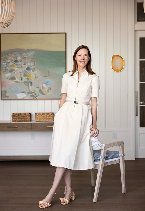 A woman in a white dress standing in a modern, well-lit room with art and decor on the walls.