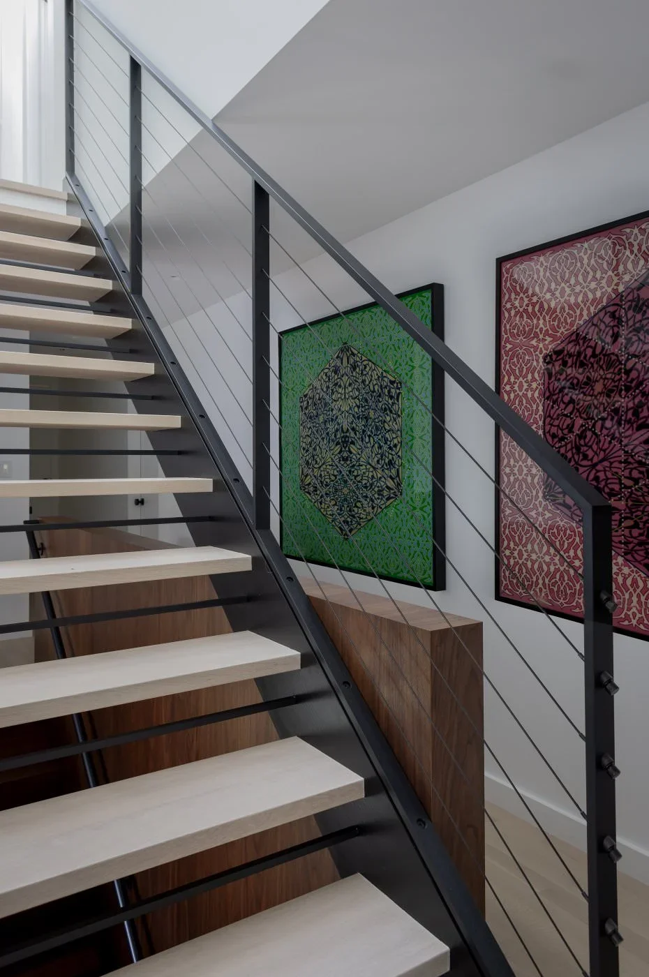 Interior view of a modern staircase with wooden steps, metal railing, and framed abstract artwork on the wall.