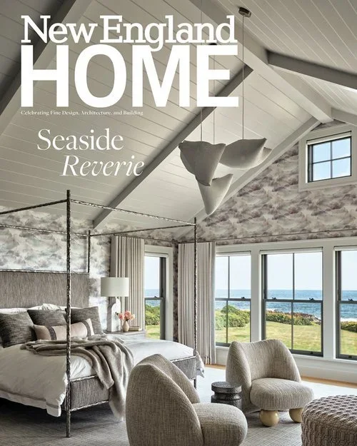 Interior of a seaside bedroom with a view of the ocean through large windows, featuring a canopy bed, modern chairs, and beach-themed décor.