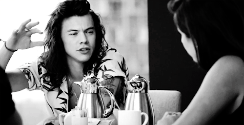A black and white animated gif of Harry Styles, with majestic hair, gesturing.