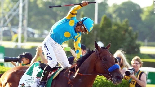 A photograph of a jockey celebrating as he rides the horse American Pharoah.