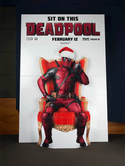 An animated gif in which Ryan Reynolds mugs against a Deadpool standee featuring an incorporated seat (so one can sit on Deadpool’s lap).