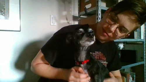 Flourish holding a very small black dog with white markings on his face and a red collar.