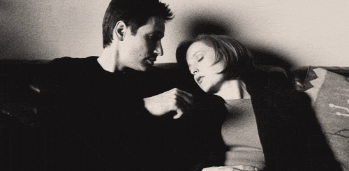 An animated gif: Mulder carefully tucks a lock of hair behind a sleeping Scully’s ear.