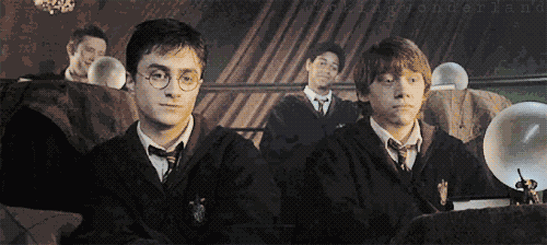 An animated gif of Ron and Harry sitting next to each other and sharing a quiet joke.
