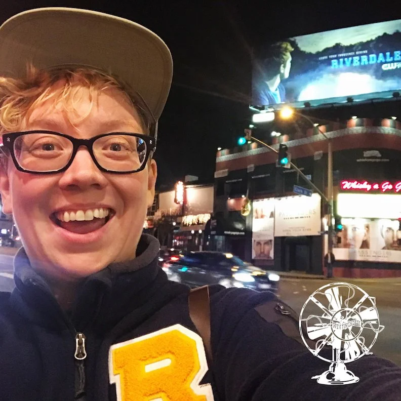 Episode 43’s cover: Britta Lundin, wearing a Riverdale letter sweater, grinning in front of a Riverdale billboard.