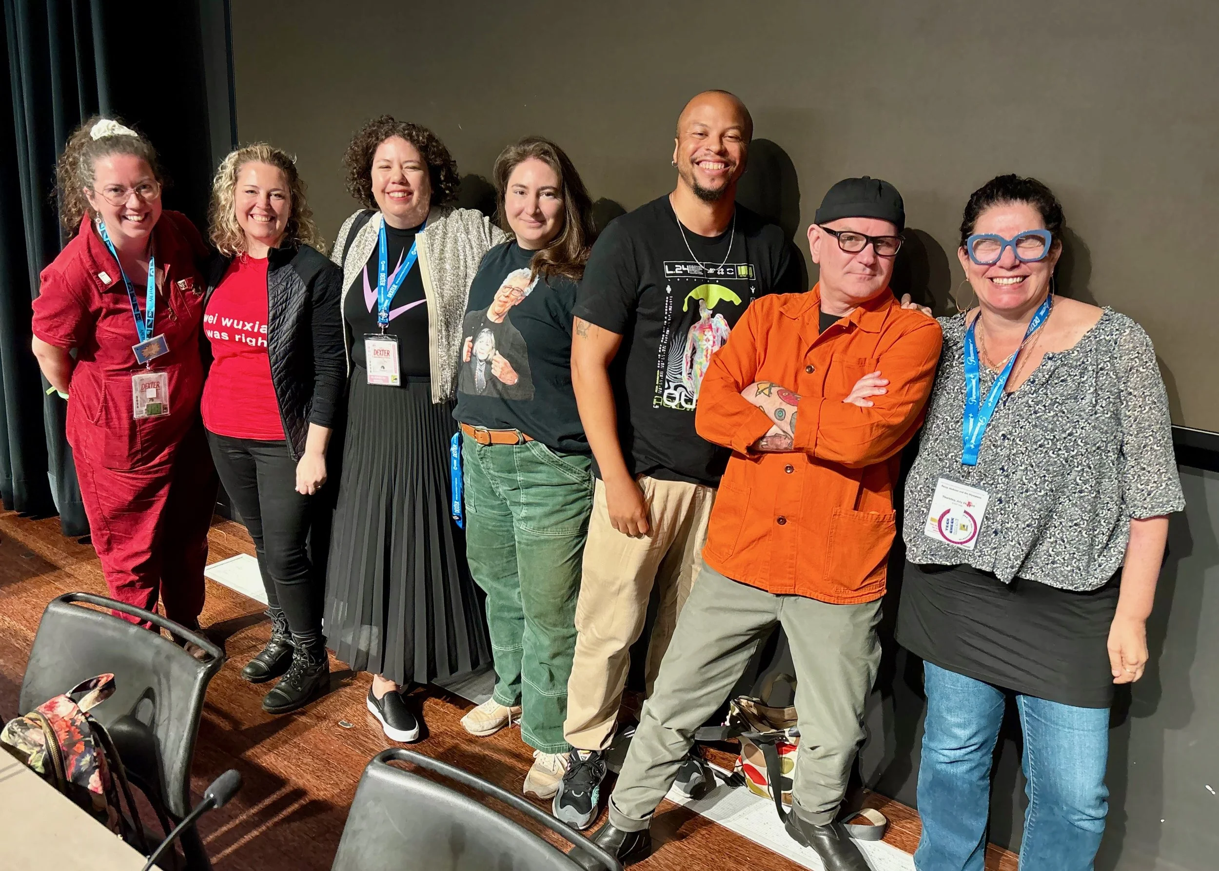 Photograph of the panelists standing on the stage: Meghan, Tessa, Elizabeth, Lin, Brent, Javi, Daphne.