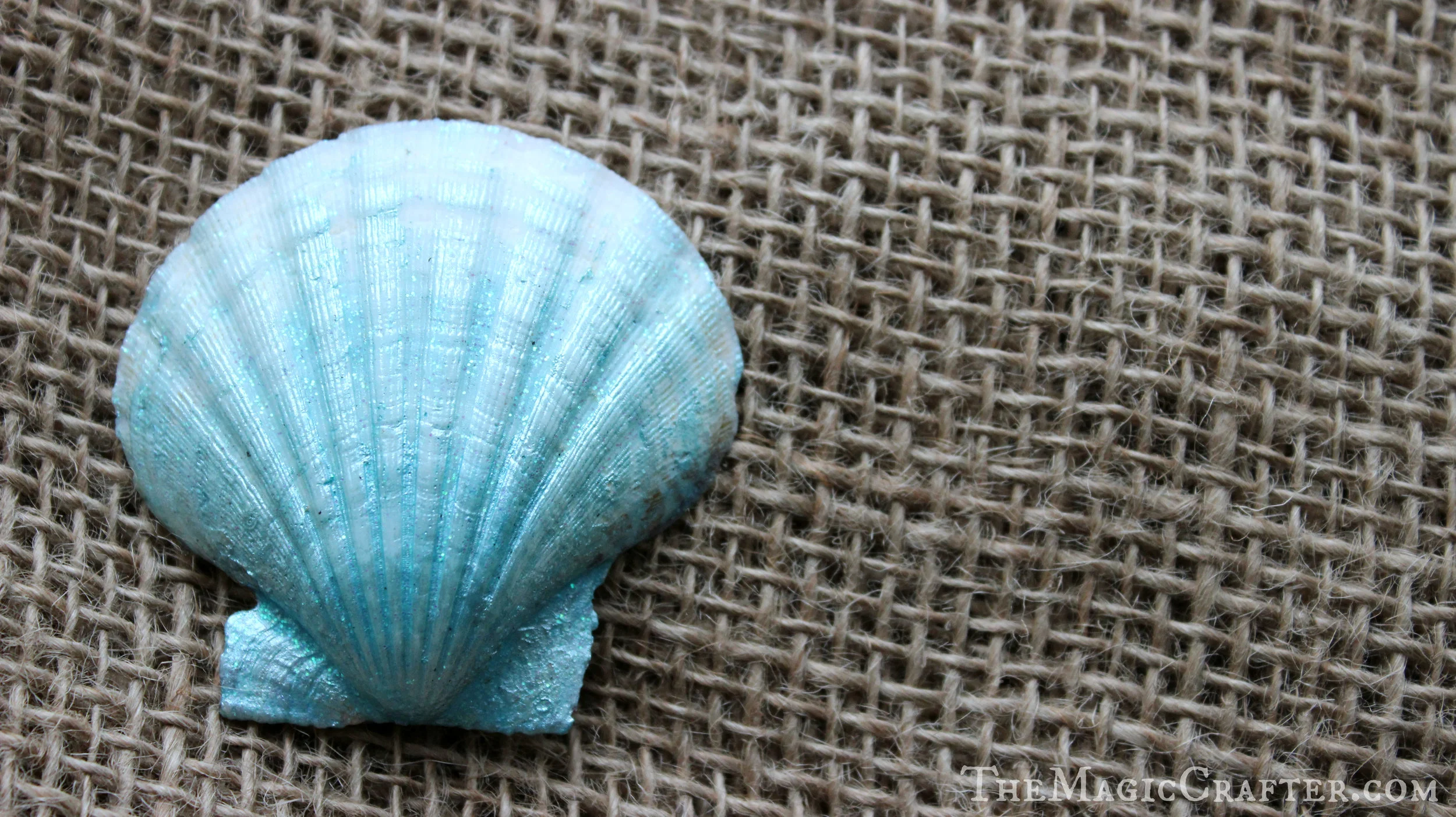 To create the neat gradient look of this shell, I lightly brushed the bottom portion of the shell with a Multi-surface Pearl acrylic crafting paint called " Aquarium " by Martha Stewart Crafts. I concentrated the color near the bottom of the seashell and then left the outer tip of it relatively bare. After that, I put some " Blueberry Slush " on the bottom of the shell and blended it out near the tip. The very tip of the seashell then got brushed with some " Sugar Cube " glitter paint. The result was a very magical looking treasure from under-the-sea. 