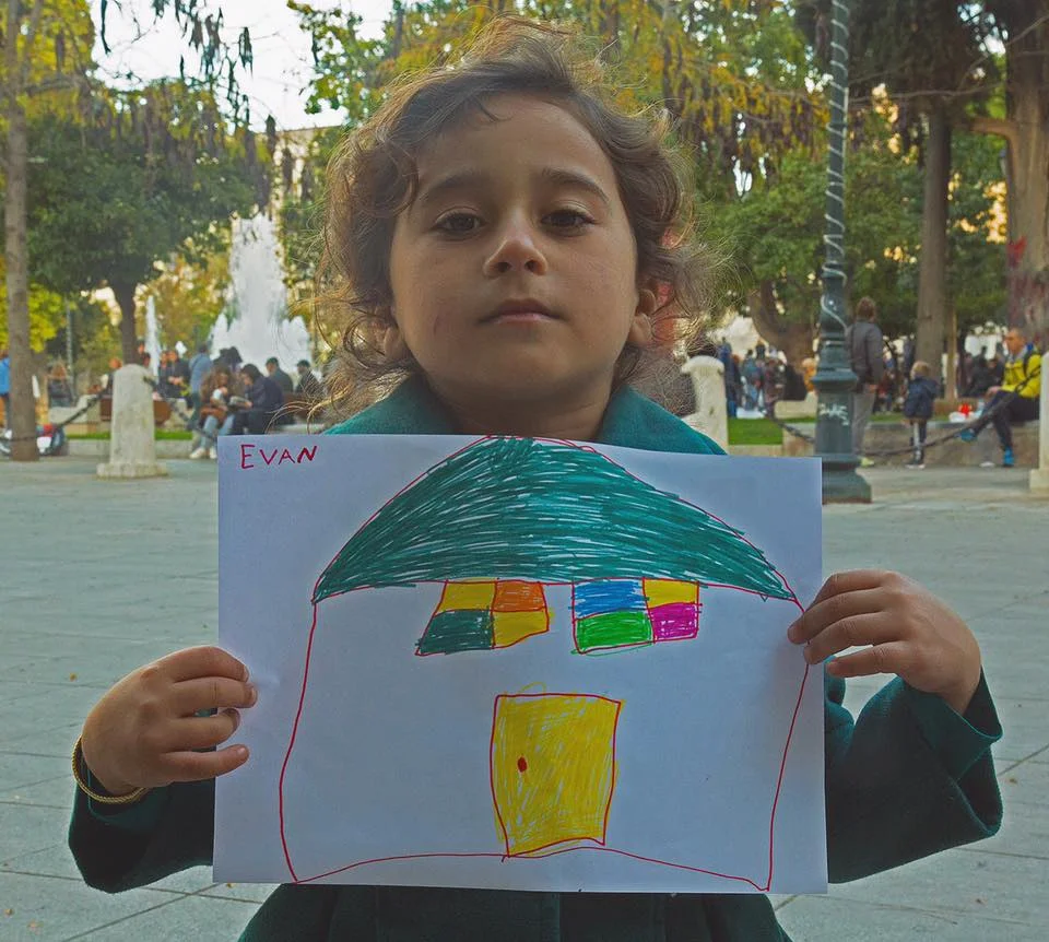 Evan, 5, Iraque “Eu quero ser professor com toda certeza. Mas o meu desenho parece mais uma casa do que uma escola, você não acha? Talvez seja por que eu ainda não tenha uma casa.” Após uma longa espera, Evan conseguiu realizar o seu sonho. Tem hoje uma casa, vive na Alemanha. “I want to be a teacher. Definitely. But my drawing looks more like a house than a school, don’t you think?! Maybe that’s because I don’t have a house yet.” After waiting for a long time, Evan saw his dream come true. They now have a new home in Germany.