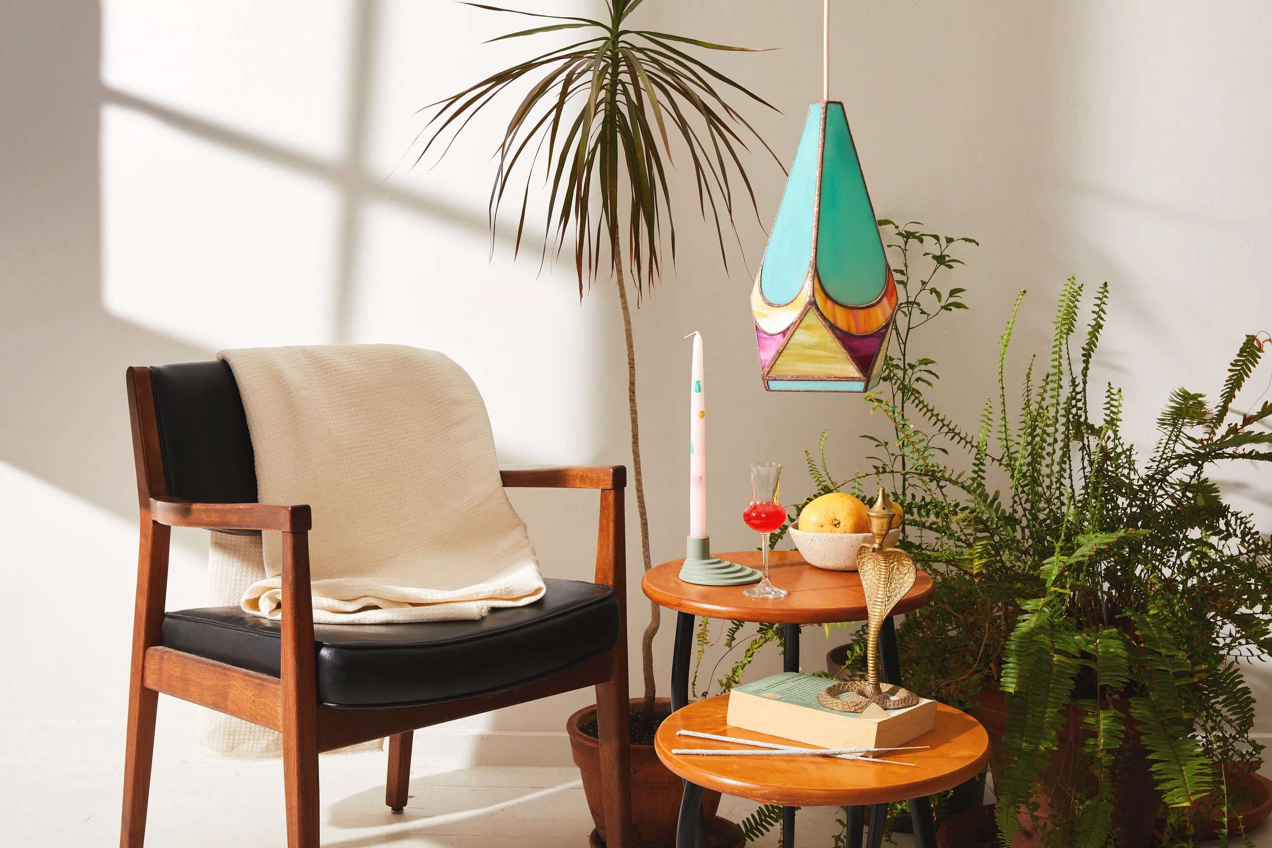Stained glass pendant light hanging above a small table next to a chair and plants.