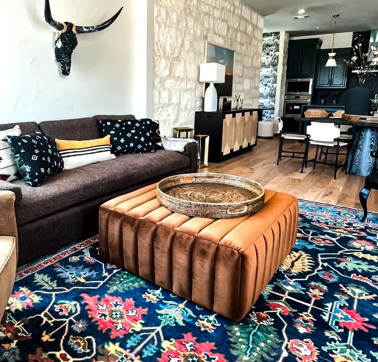 Residential living room with longhorn wall decor, navy Persian rug, and caramel channeled ottoman by Kara Legako Design, Dallas TX
