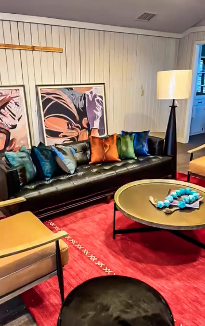 Bold living room with black tufted leather sofa, vibrant silk pillows, red rug, and oversized pop art by Kara Legako Design, Dallas TX