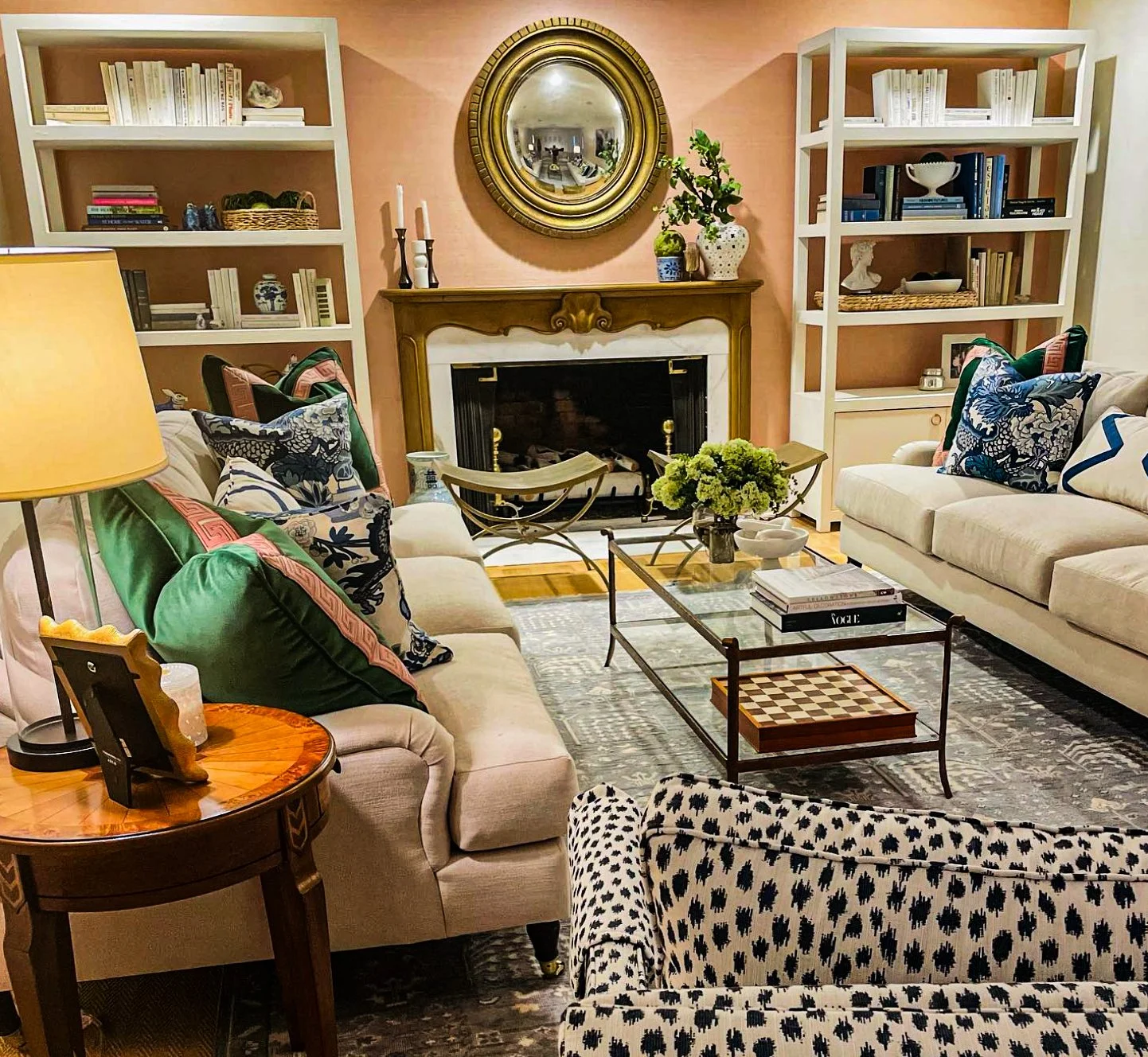 Traditional living room with salmon walls, gold convex mirror, built-in bookshelves, and fireplace by Kara Legako Design, Dallas TX