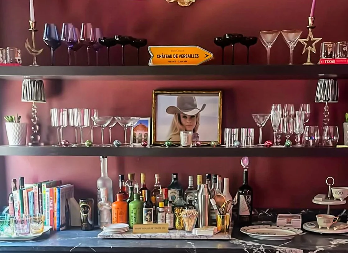 Residential bar with deep burgundy walls, styled glassware shelves, and curated bar accessories by Kara Legako Design, Dallas TX