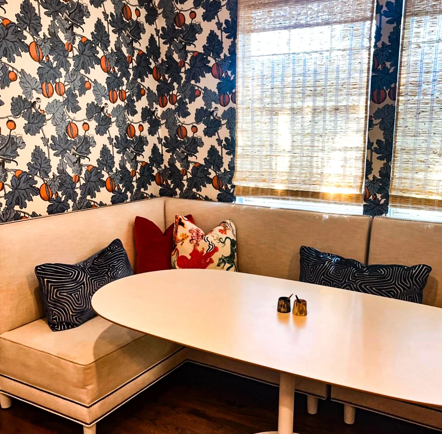 Dining banquette with cream linen seating, bold botanical wallpaper, and woven shades by Kara Legako Design, Dallas TX