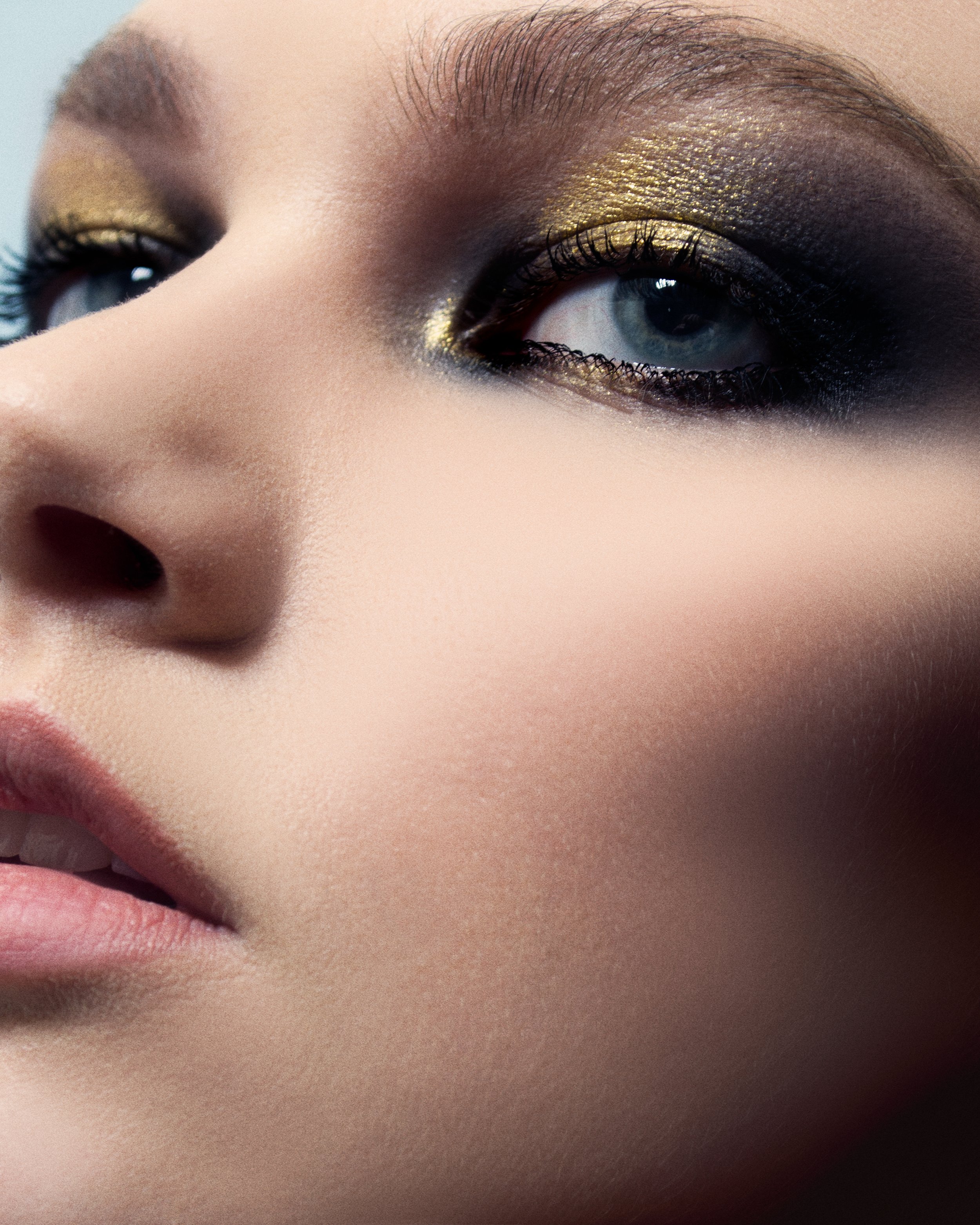 Close-up of a person's eye with gold metallic eyeshadow and black mascara.