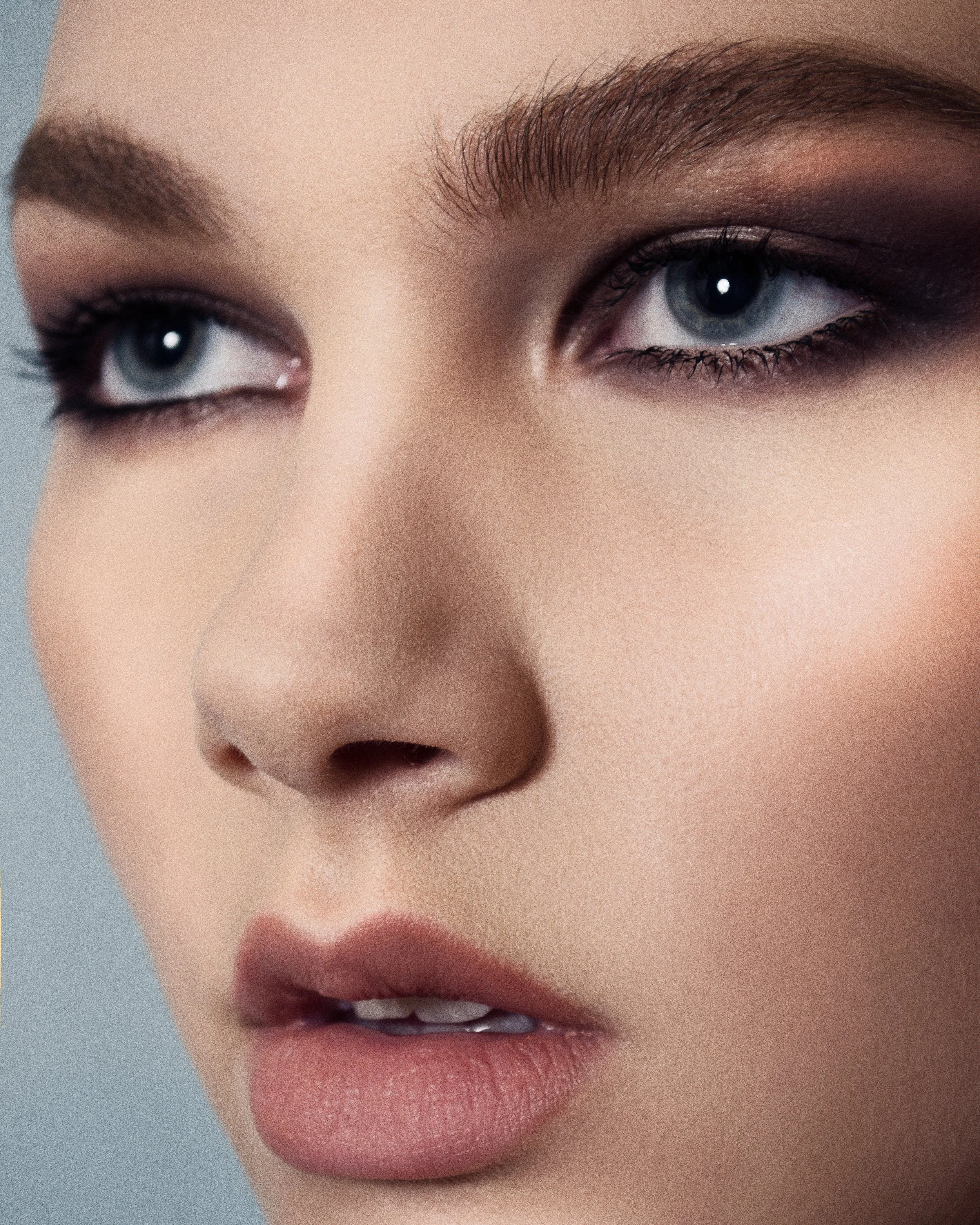 Close-up of a person's face showing blue eyes, well-groomed eyebrows, and pink lips, with a neutral facial expression.