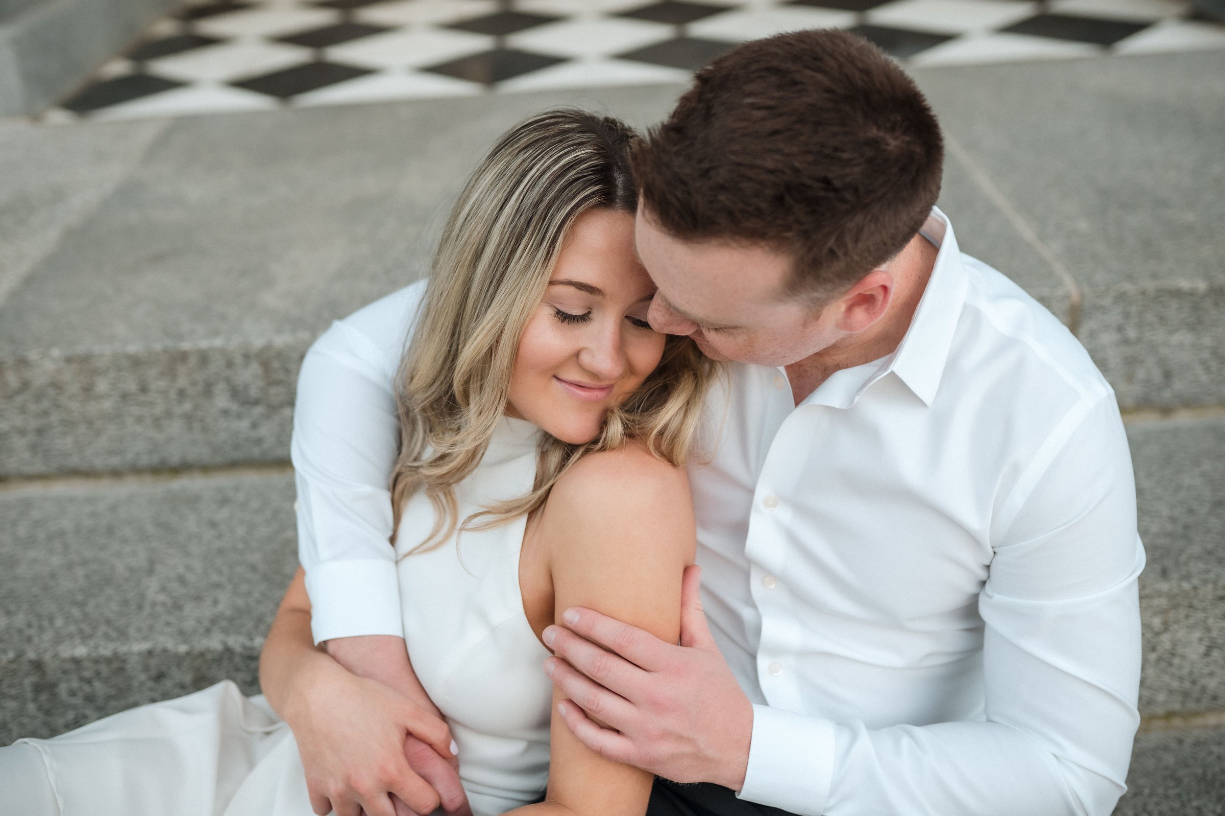 A young couple sitting closely together on the steps at the Sacramento Capitol, sharing an intimate moment during their engagement session. Photography by Katherine Nicole Photography.