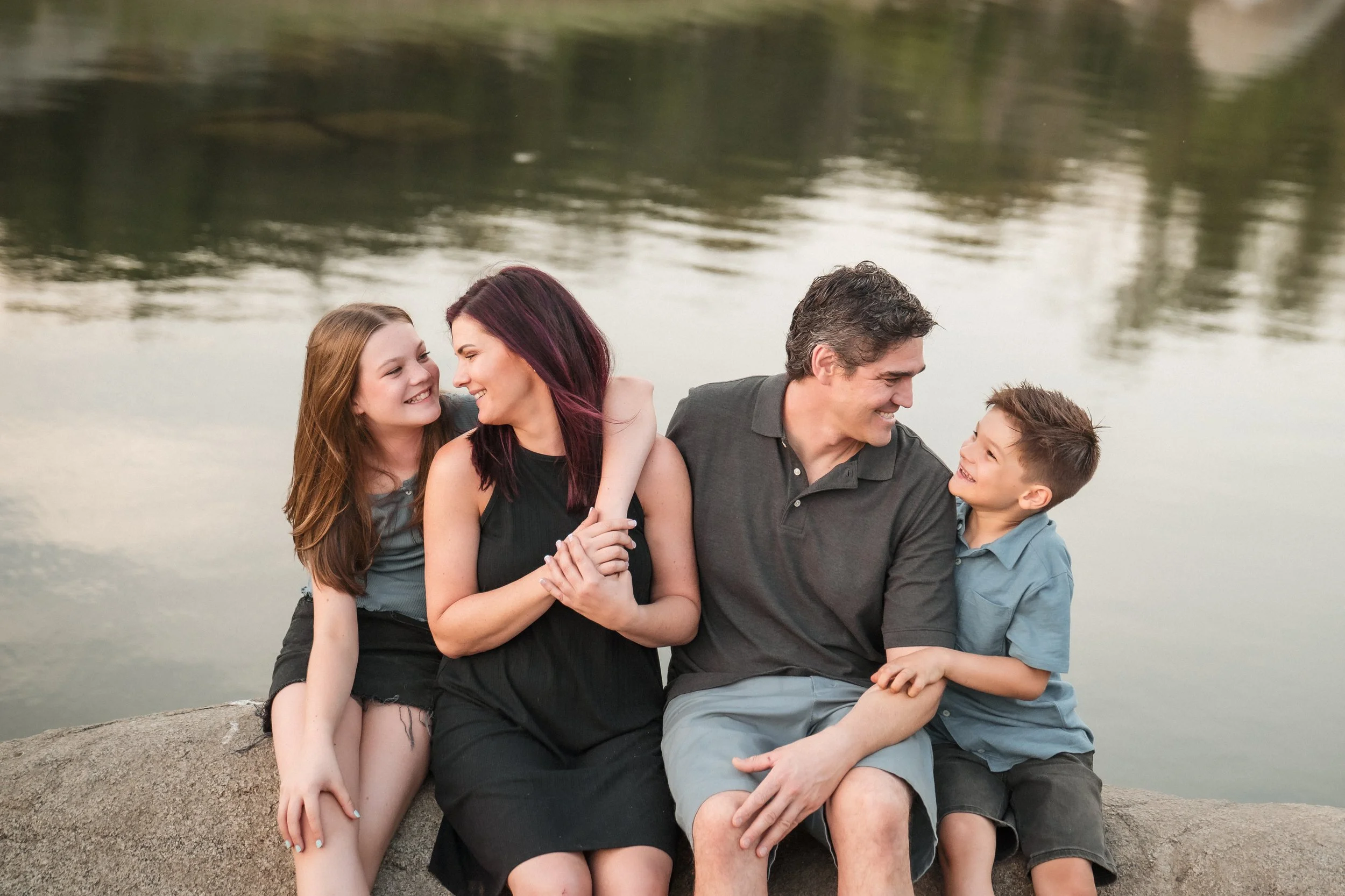 A family sits on a rock by the lake during their family photos, with Sacramento Family Photographer, Katherine Nicole Photography