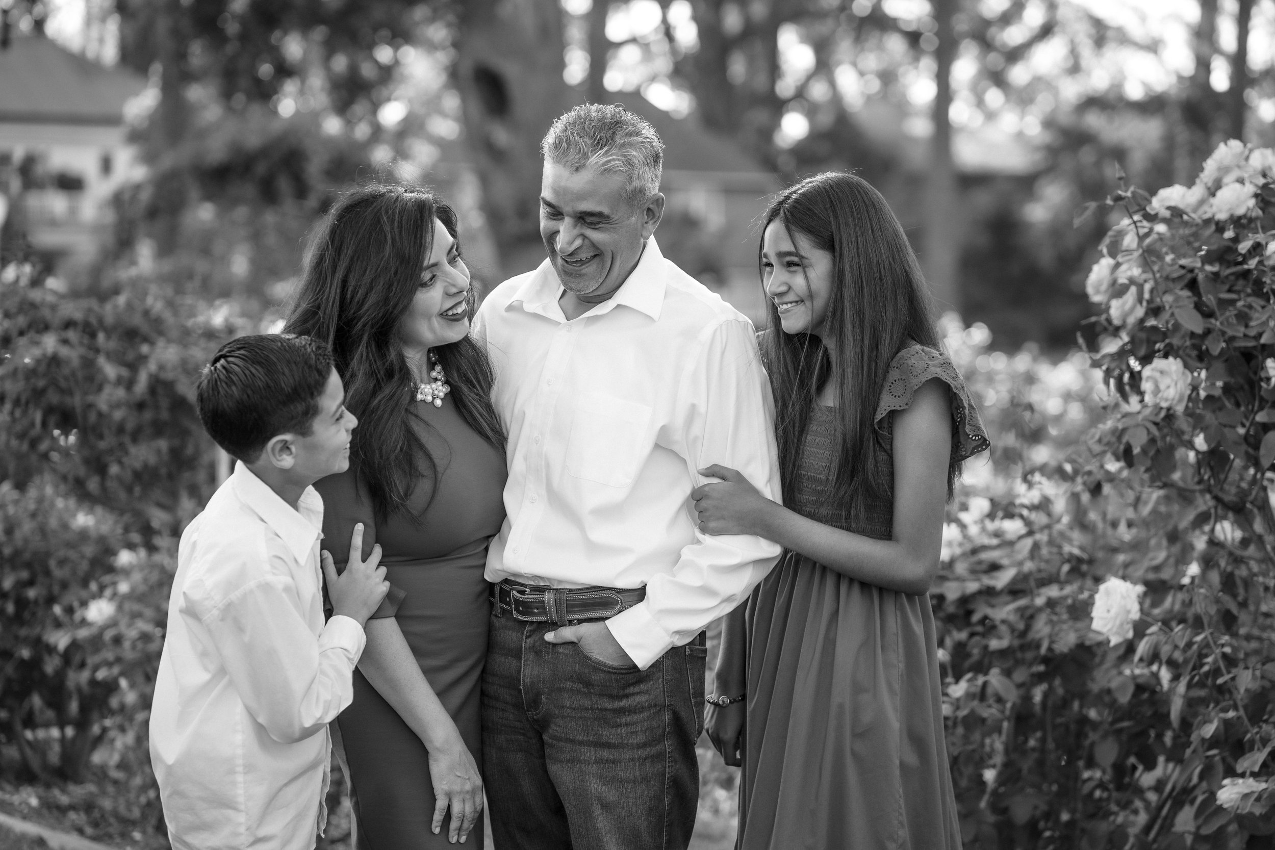 A black and white photo of a group of five people, three women and two men, smiling during family photos at the McKinley Park rose garden with Sacramento family photographer, Katherine Nicole Photography.
