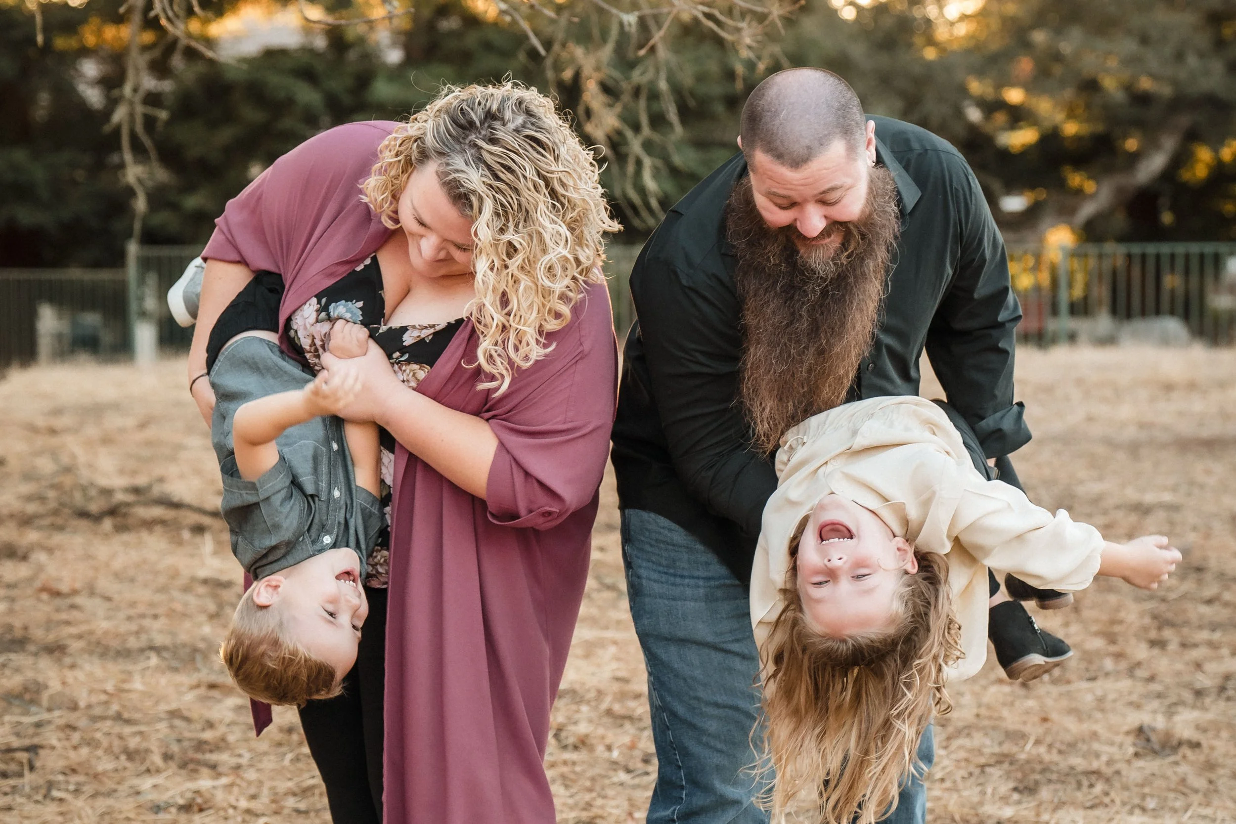 A family having fun outdoors, playing and laughing on a wooded park ground during sunset while taking family photos with Sacramento family photographer Katherine Nicole Photography. 