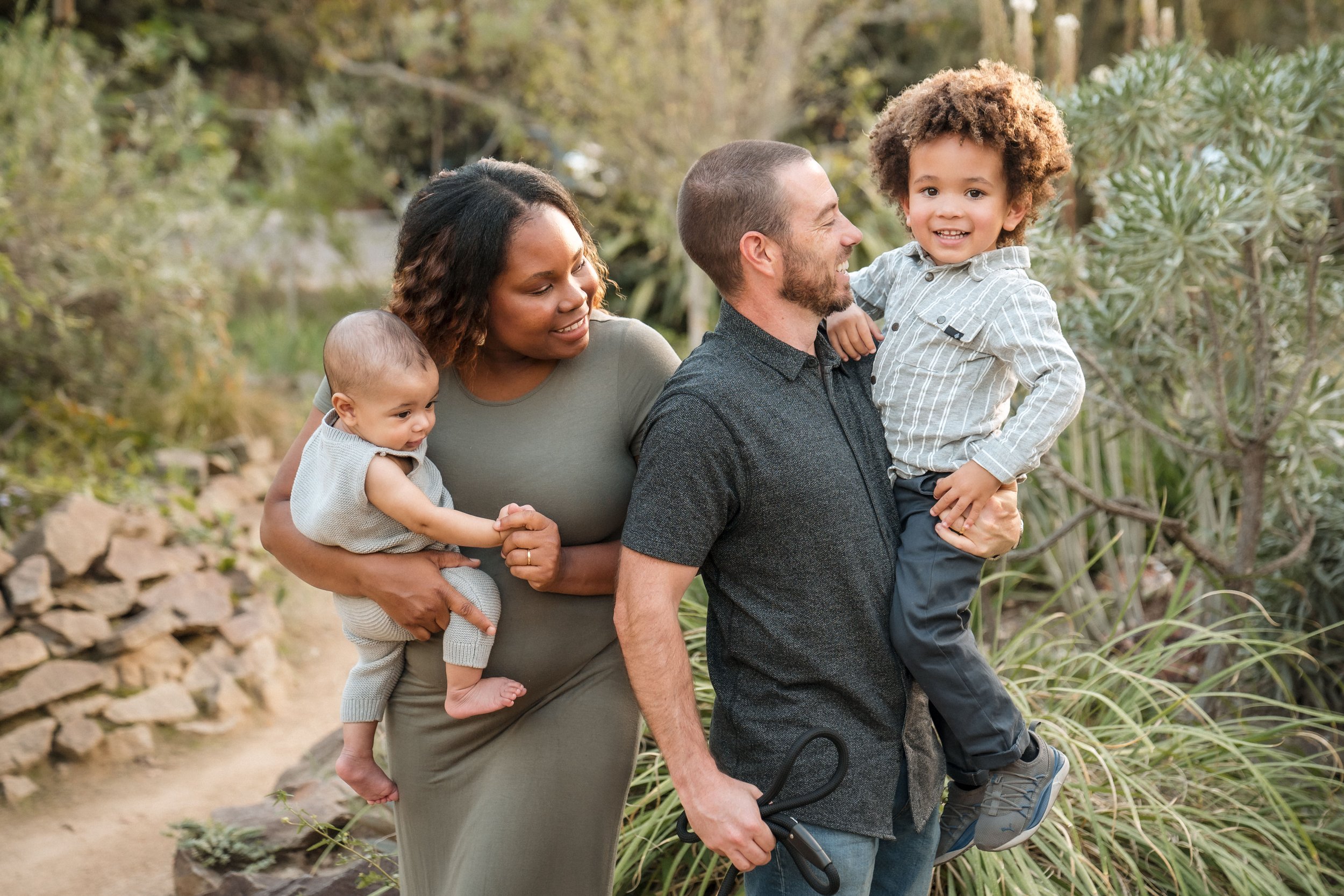 A family of four enjoying a walk outdoors in a natural setting, with trees and rocks visible in the background, during a family photo session with Sacramento family photographer Katherine Nicole Photography. 