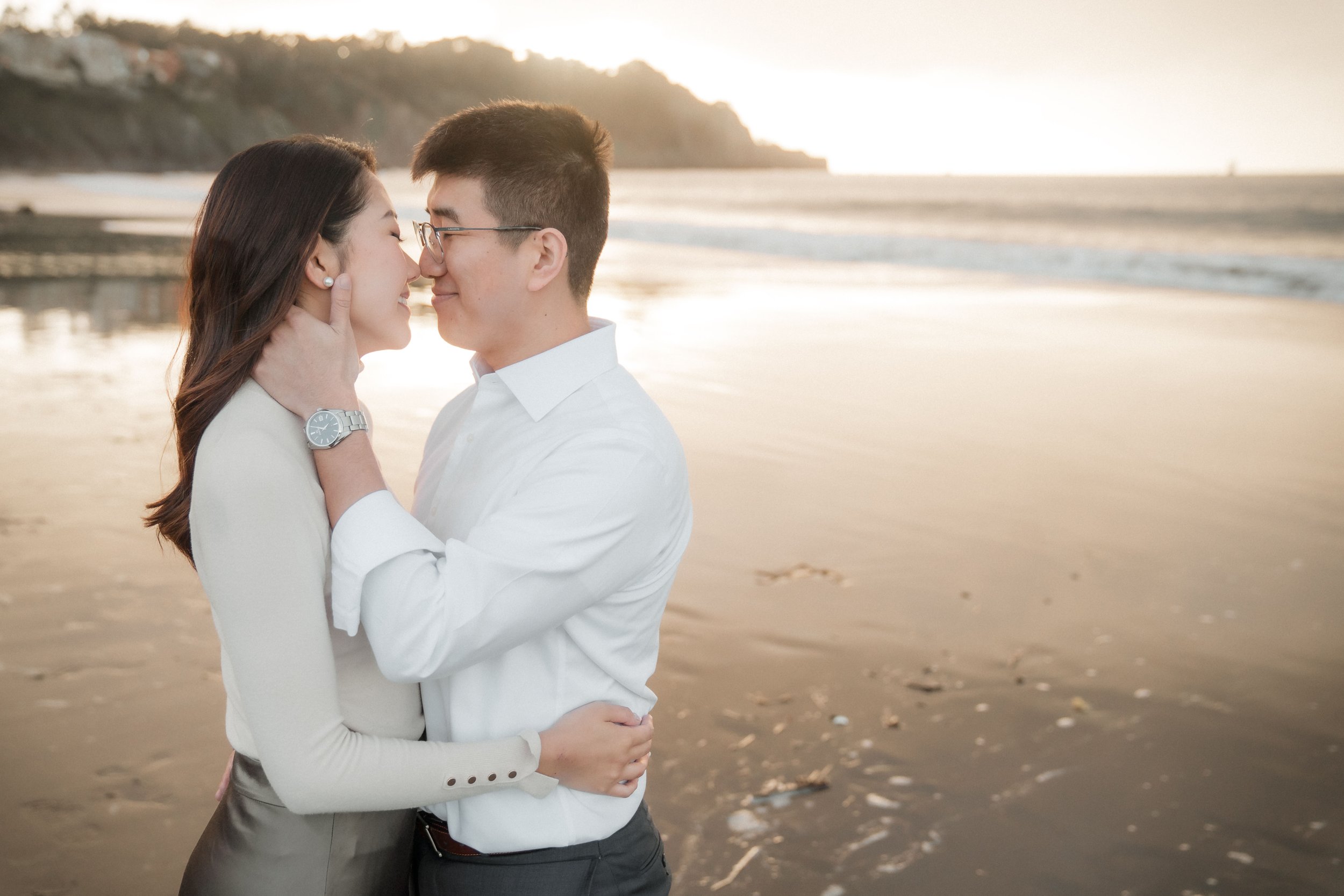 A couple, embracing and touching noses on Baker Beach, during their Bay Area engagement session. Photography by Katherine Nicole Photography.