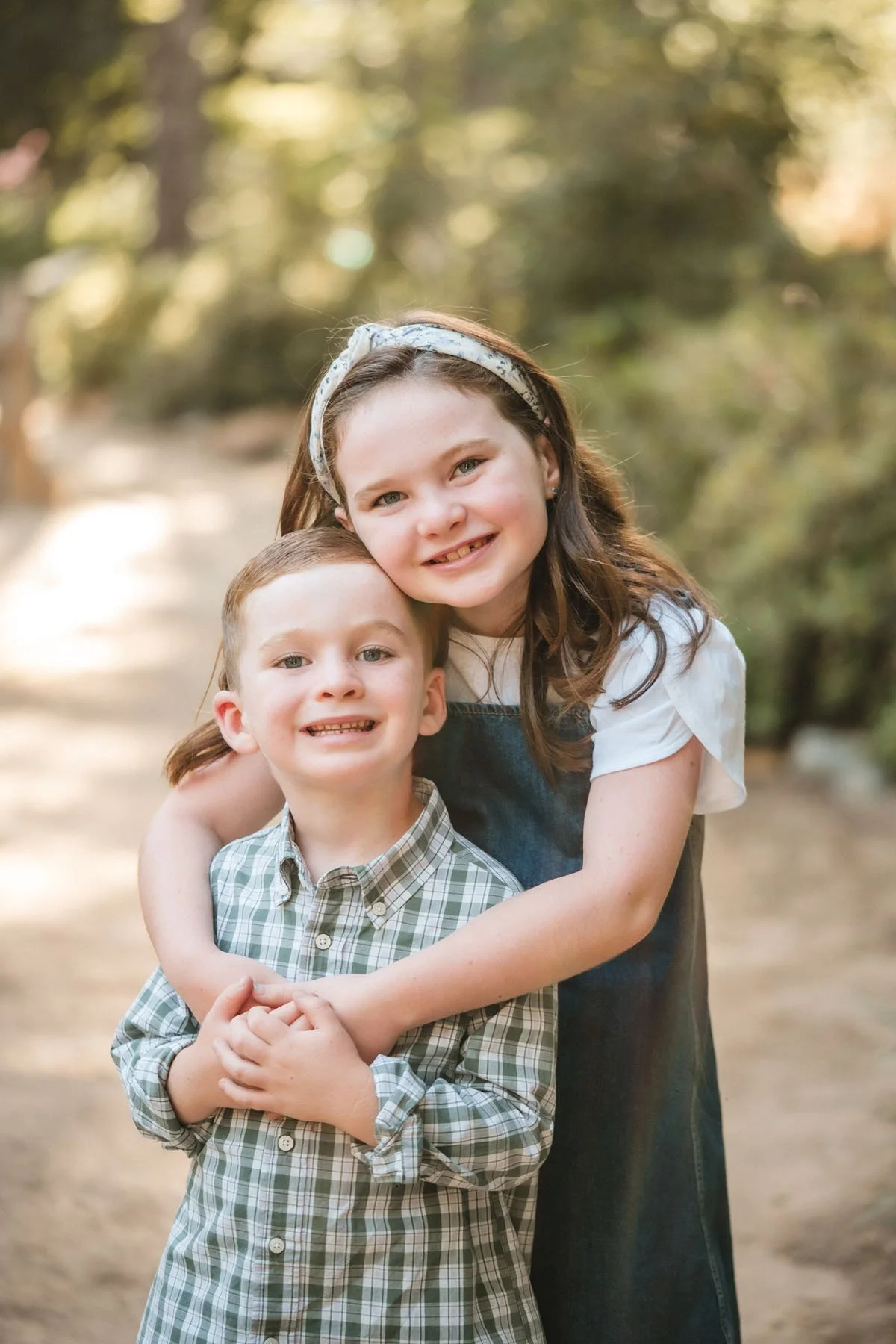 Two children, a girl and a boy, hugging outdoors with trees in the background. Family photos at Jensen Botanical Garden with Sacramento family photographer, Katherine Nicole Photography.