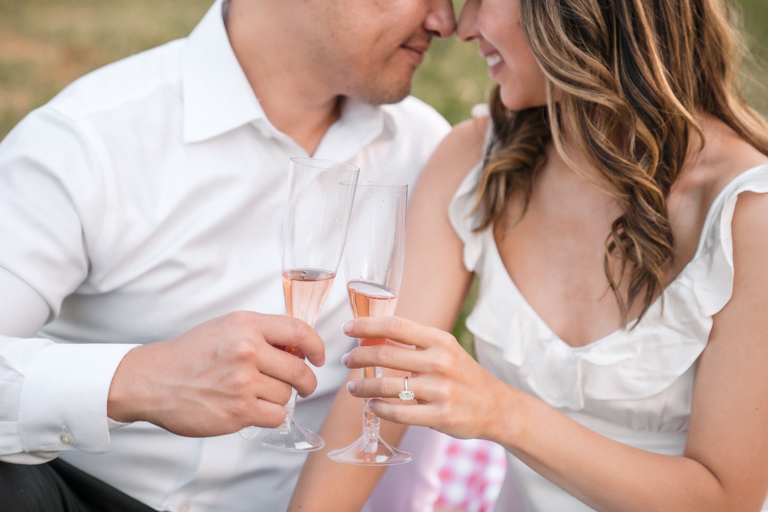 A couple touching foreheads, smiling, and holding glasses of rosé wine during their engagement session with Katherine Nicole Photography.