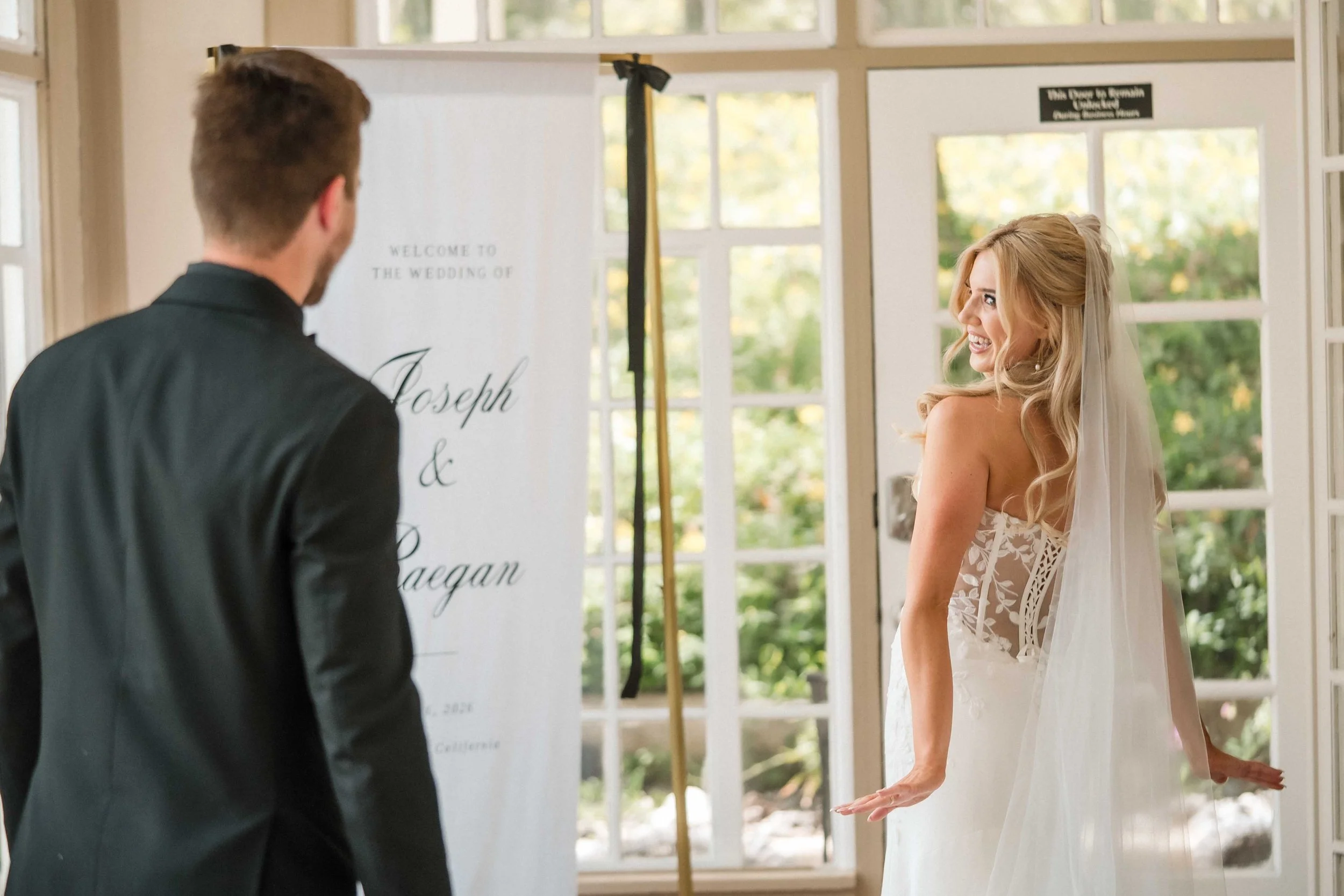A bride and groom during their first look at the Monte Verde Inn, with a wedding sign and large windows in the background. Photography by Sacramento wedding photographer Katherine Nicole Photography.