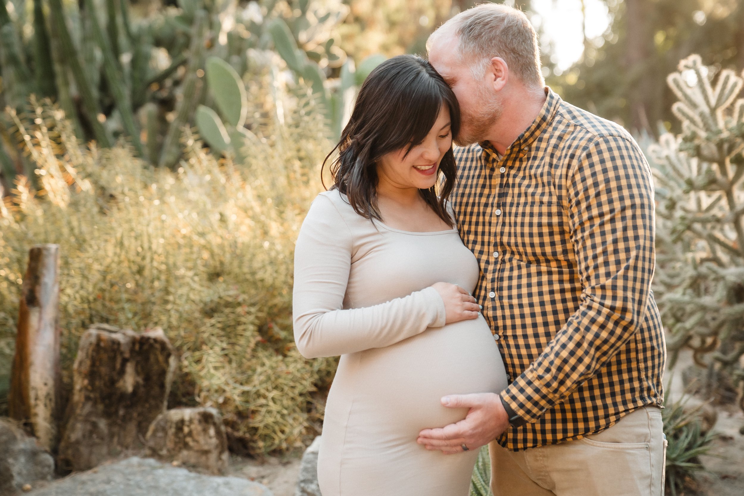 Pregnant woman and man sharing a tender moment outdoors with a cactus and trees in the background, while taking maternity photos with Sacramento family photographer Katherine Nicole Photography. 