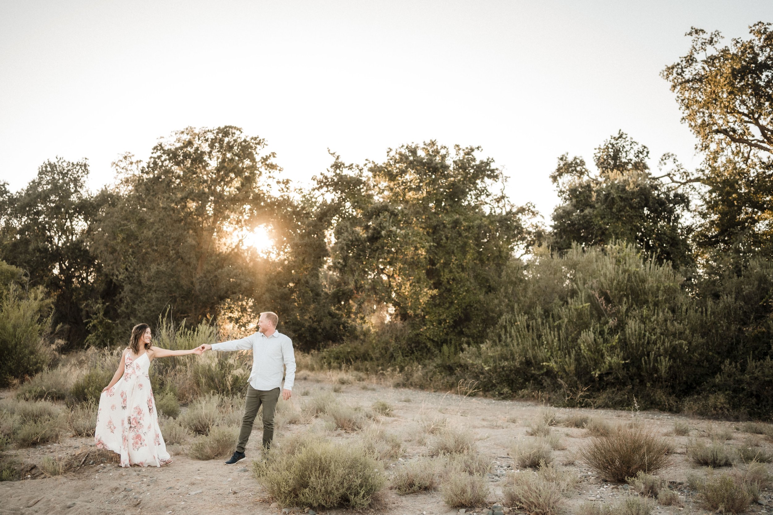A couple holding hands in a natural outdoor setting at sunset, surrounded by trees and bushes during their Sacramento engagement session. Photography by Katherine Nicole Photography.
